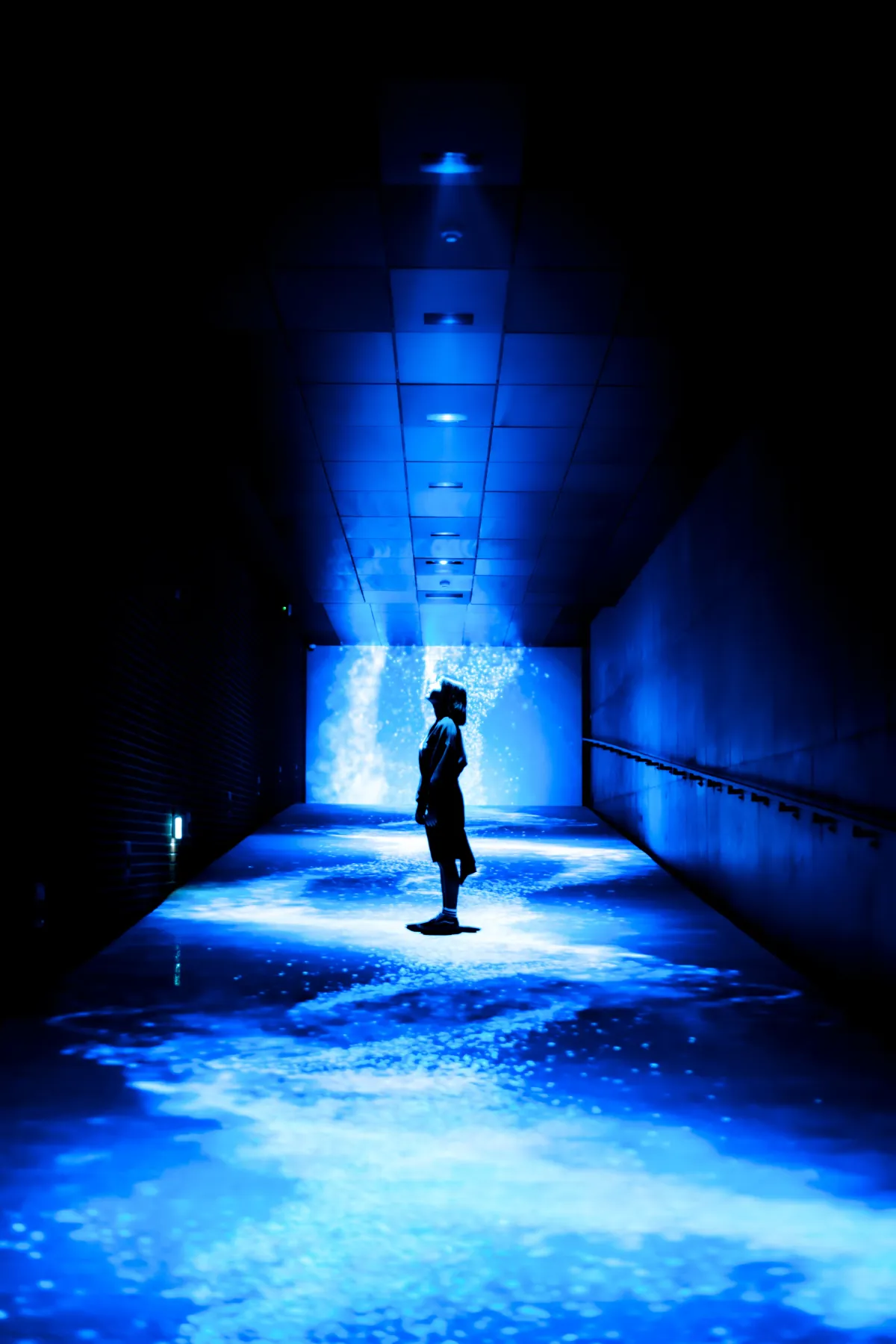 A mysterious silhouette stands in a futuristic blue-lit corridor in Seoul, South Korea.